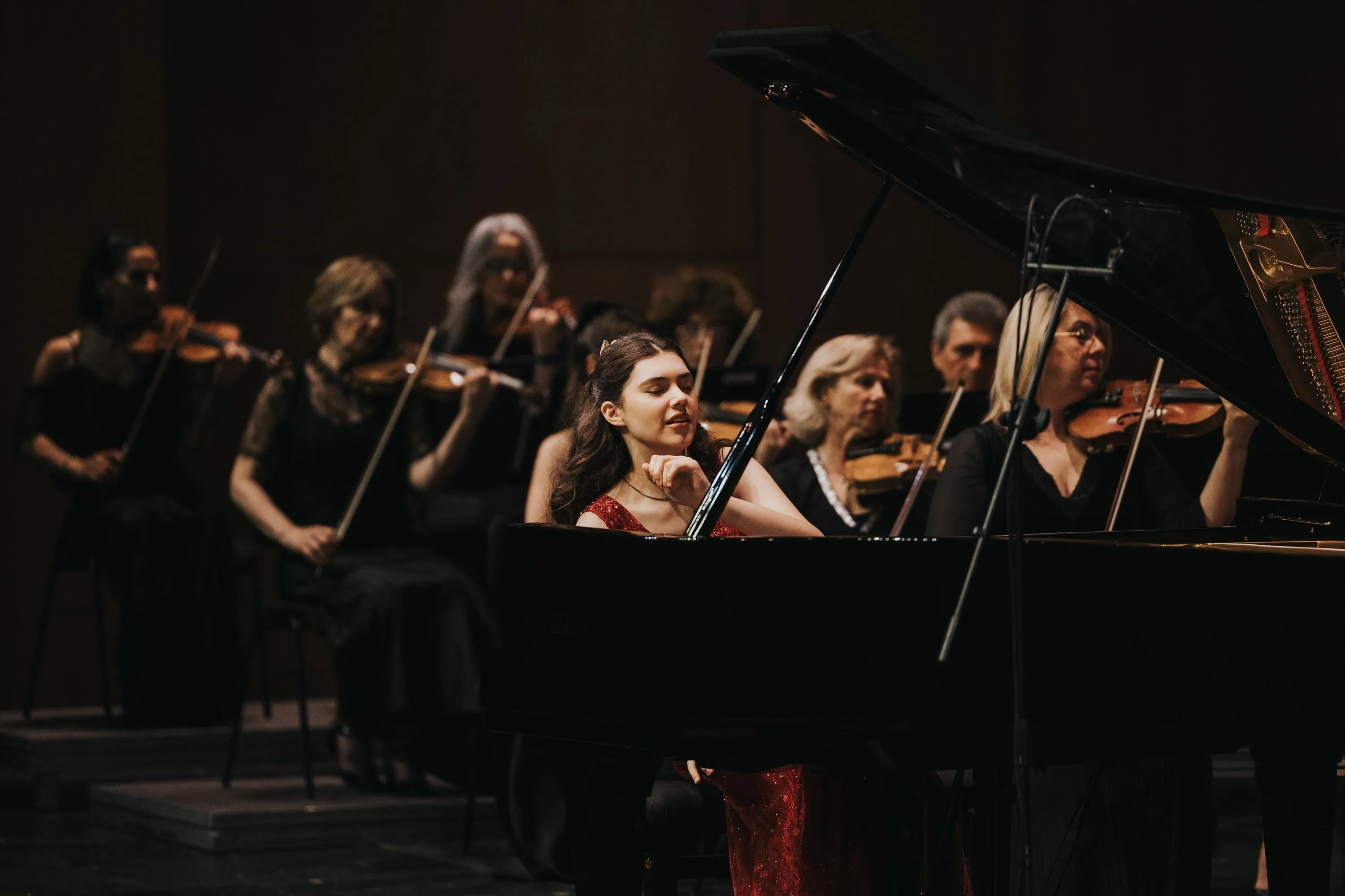 İlyun Bürkev playing the piano on stage in front of the string section of an orchestra